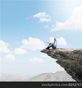 Success in business. Young businessman sitting on edge of rock mountain and using tablet pc