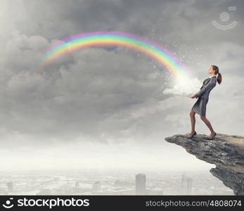 Success in business. Young businesswoman on rock edge and colorful rainbow