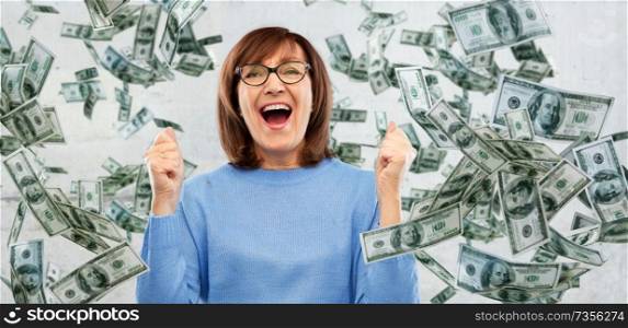 success, jackpot and finances people concept - happy laughing senior woman in glasses celebrating triumph under money falling from above over grey background. happy senior woman celebrating success over money