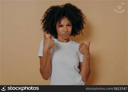 Success sign. Confident young african woman showing thumbs up with both hands and looking at camera isolated on beige background, showing winner gesture and smiling. Body language concept. Confident young african woman showing thumbs up with both hands while standing on beige background