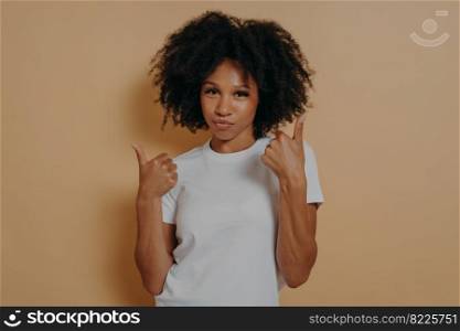 Success sign. Confident young african woman showing thumbs up with both hands and looking at camera isolated on beige background, showing winner gesture and smiling. Body language concept. Confident young african woman showing thumbs up with both hands while standing on beige background
