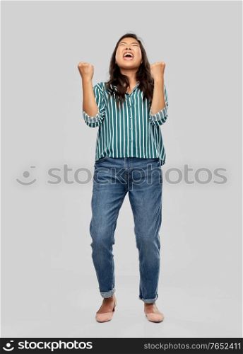 success, winning gesture and people concept - happy young asian woman celebrating victory over grey background. happy young asian woman celebrating success