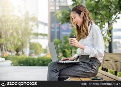 Successful Asian business young woman working laptop outdoor corporate building exterior, Happy professional smiling businesswoman sitting alone typing computer outside street city near office
