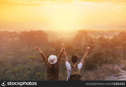 Successful Asian couple open arms on sunrise mountain peak. Happy Man and Woman traveler celebrating with holding hands together. Rear view.