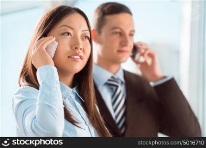 Successful business people talking on cell phone while standing at office or hallway