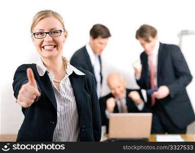 Successful business woman standing in front of her colleagues; selective focus on woman