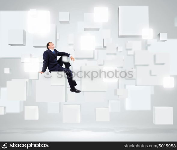 Successful business. Young businessman sitting on white cube in white room