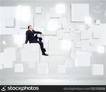 Successful business. Young businessman sitting on white cube in white room