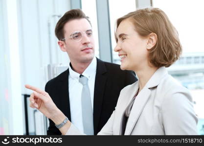 Successful businessman and businesswoman writing good ideas on sticky notes pasted on glass wall in modern office meeting.