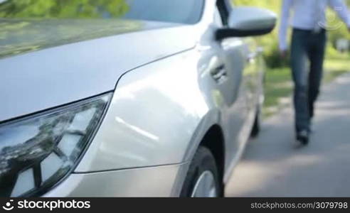 Successful businessman in formal wear getting into parked car on the roadside. Stylish handsome man in necktie stepping into modern vehicle while making business trip in summer. Slow motion. Steadicam stabilized shot.