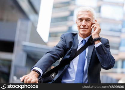 Successful businessman on bicycle with mobile phone. Successful businessman on bicycle in city holding mobile phone