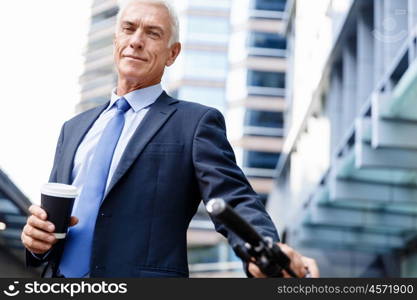 Successful businessman riding bicycle. Successful businessman in suit riding bicycle and holding coffee