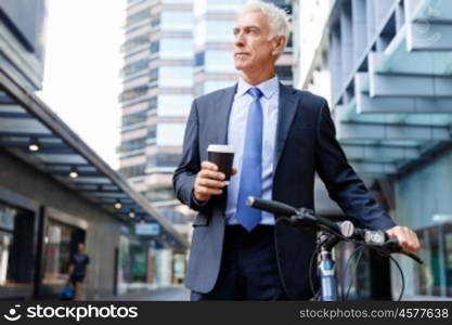 Successful businessman riding bicycle. Successful businessman in suit riding bicycle and holding coffee