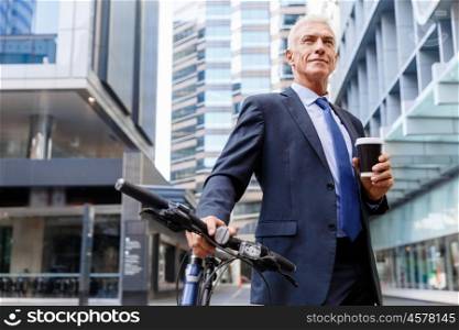 Successful businessman riding bicycle. Successful businessman in suit riding bicycle and holding coffee