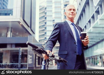 Successful businessman riding bicycle. Successful businessman in suit riding bicycle and holding coffee