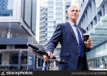 Successful businessman riding bicycle. Successful businessman in suit riding bicycle and holding coffee