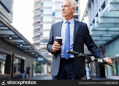 Successful businessman riding bicycle. Successful businessman in suit riding bicycle and holding coffee