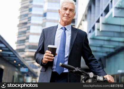 Successful businessman riding bicycle. Successful businessman in suit riding bicycle and holding coffee