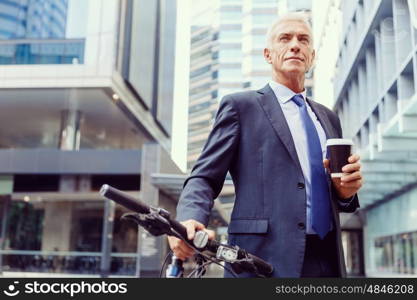 Successful businessman riding bicycle. Successful businessman in suit riding bicycle and holding coffee