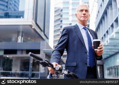 Successful businessman riding bicycle. Successful businessman in suit riding bicycle and holding coffee