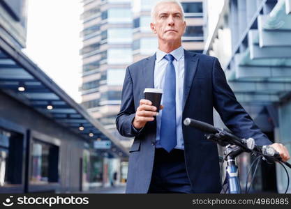 Successful businessman riding bicycle. Successful businessman in suit riding bicycle and holding coffee