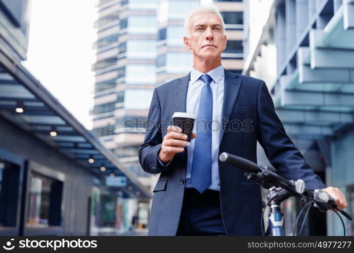 Successful businessman riding bicycle. Successful businessman in suit riding bicycle and holding coffee