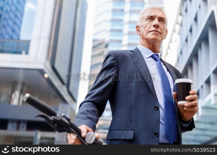 Successful businessman riding bicycle. Successful businessman in suit riding bicycle and holding coffee