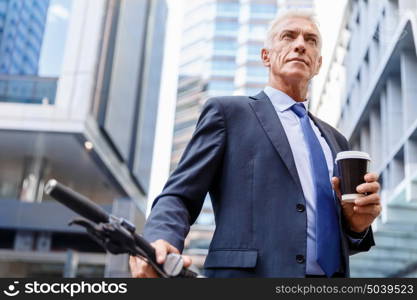 Successful businessman riding bicycle. Successful businessman in suit riding bicycle and holding coffee