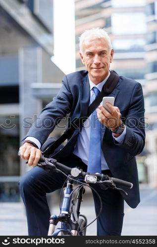 Successful businessman riding bicycle. Successful businessman in suit riding bicycle and holding mobile phone