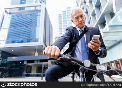 Successful businessman riding bicycle. Successful businessman in suit riding bicycle and holding mobile phone