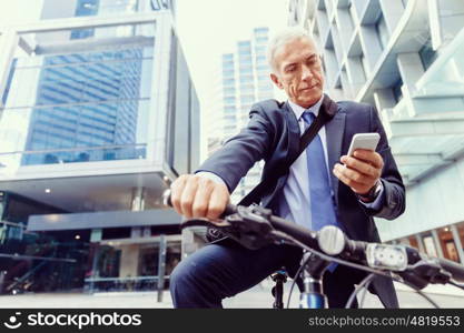 Successful businessman riding bicycle. Successful businessman in suit riding bicycle and holding mobile phone