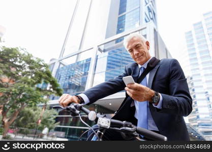 Successful businessman riding bicycle. Successful businessman in suit riding bicycle and holding mobile phone