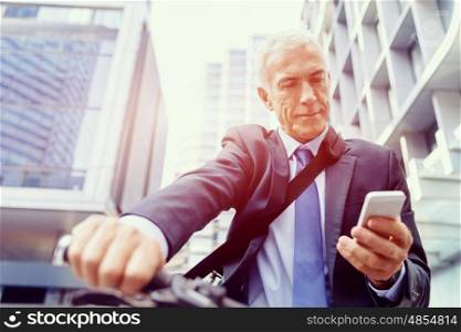 Successful businessman riding bicycle. Successful businessman in suit riding bicycle and holding mobile phone