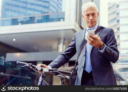 Successful businessman riding bicycle. Successful businessman in suit riding bicycle and holding mobile phone