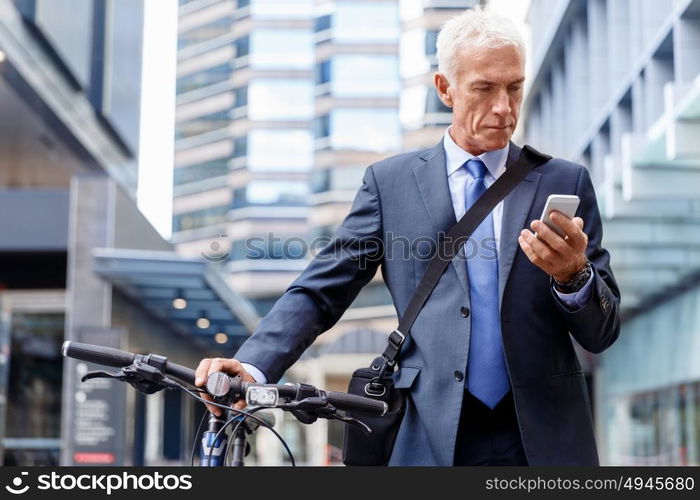 Successful businessman riding bicycle. Successful businessman in suit riding bicycle and holding mobile phone