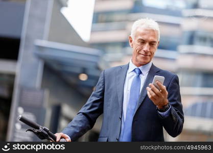 Successful businessman riding bicycle. Successful businessman in suit riding bicycle and holding mobile phone