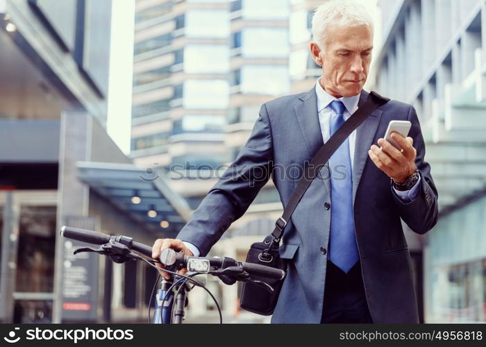 Successful businessman riding bicycle. Successful businessman in suit riding bicycle and holding mobile phone