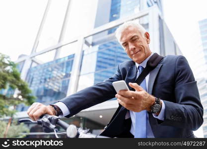 Successful businessman riding bicycle. Successful businessman in suit riding bicycle and holding mobile phone