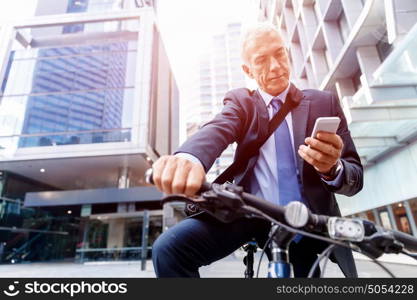 Successful businessman riding bicycle. Successful businessman in suit riding bicycle and holding mobile phone