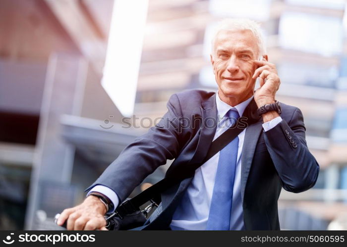 Successful businessman riding bicycle. Successful businessman in suit riding bicycle and holding mobile phone