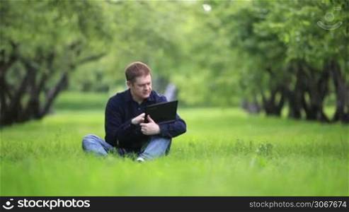 Successful businessman working with notebook in the park sitting on green grass.