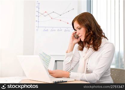 Successful businesswoman at office on phone working with laptop