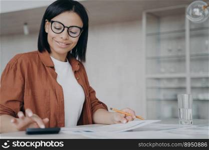 Successful businesswoman is calculating expends. Friendly young mixed race woman in glasses, entrepreneur is working remote. Workplace at home on quarantine. Finances and investment concept.. Successful mixed race businesswoman is calculating expends. Finances and investment concept.