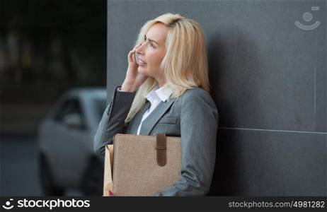 Successful businesswoman or entrepreneur talking on cellphone while standing outdoor. City business woman working.