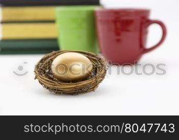 Successful, collaborative investment reflected in two coffee mugs, red and green, and books combined with selective focus on gold nest egg. Education, due diligence. and smart, winning strategy reflected in symbols.