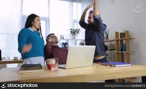 Successful entrepreneurs and business people achieving goals. Young diverse business team in casual outfits celebrating success together at workplace in office and giving high-five. Dolly shot.