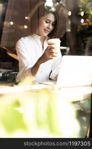 Successful female young adult asian freelancer working in cafe with laptop and coffee cup.