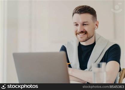 Successful male freelancer having web conference with colleagues using earphones and laptop, being happy to hear good news, cheerful businessman in casual wear talking trough video call in office. Happy businessman having video call on laptop while working at home