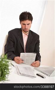 Successful modern businessman with laptop and newspaper sitting at the office
