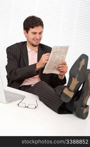 Successful modern businessman with laptop and newspaper sitting at the office